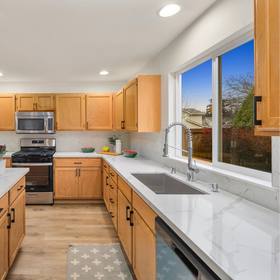 Bright remodeled kitchen with natural wood cabinets, white countertops, stainless sink and stove